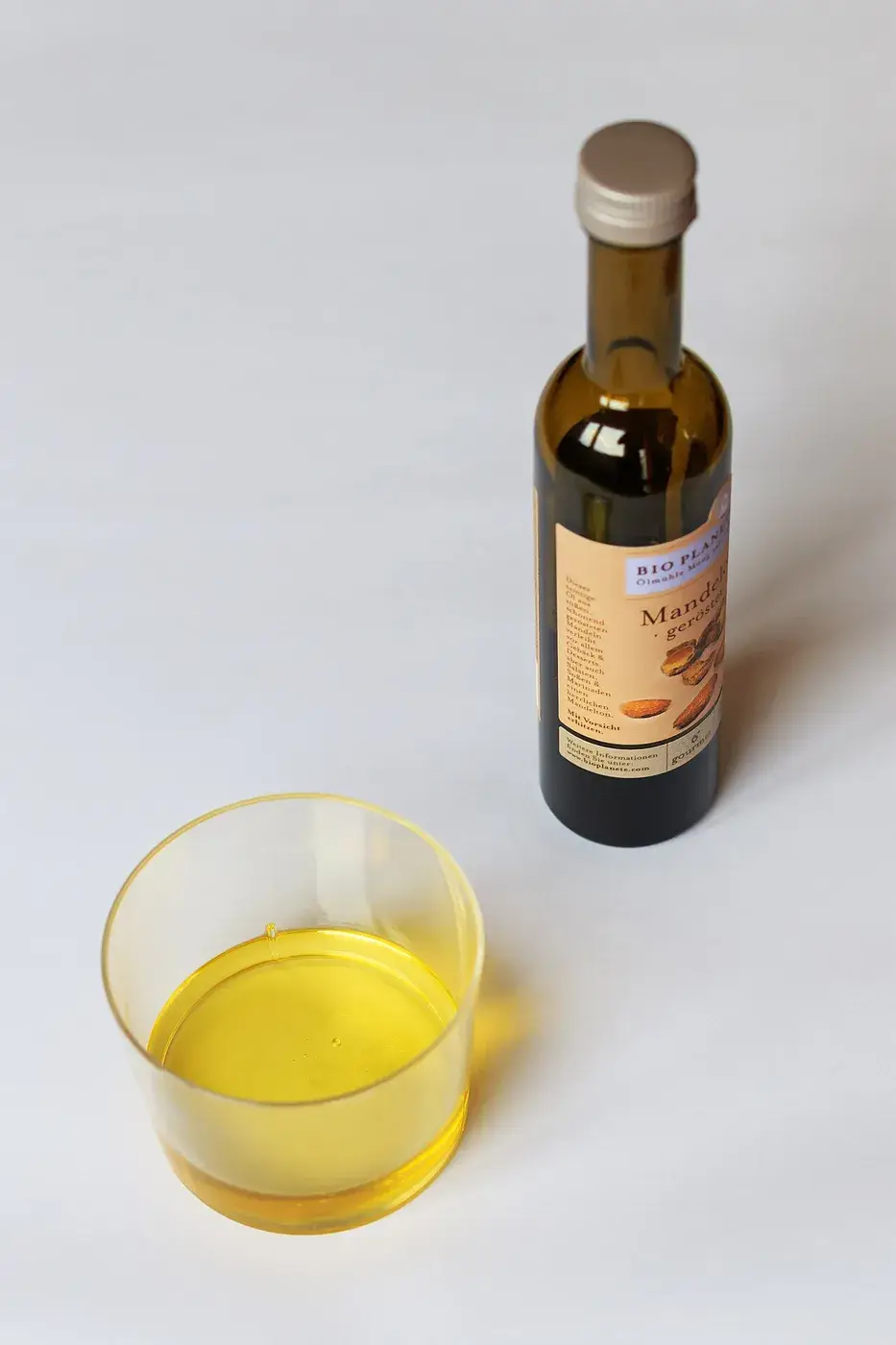 A small bottle of almond oil beside a glass of the oil