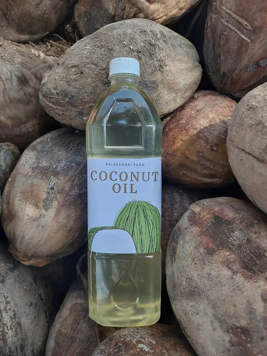 A clear bottle of coconut oil standing among dried coconuts