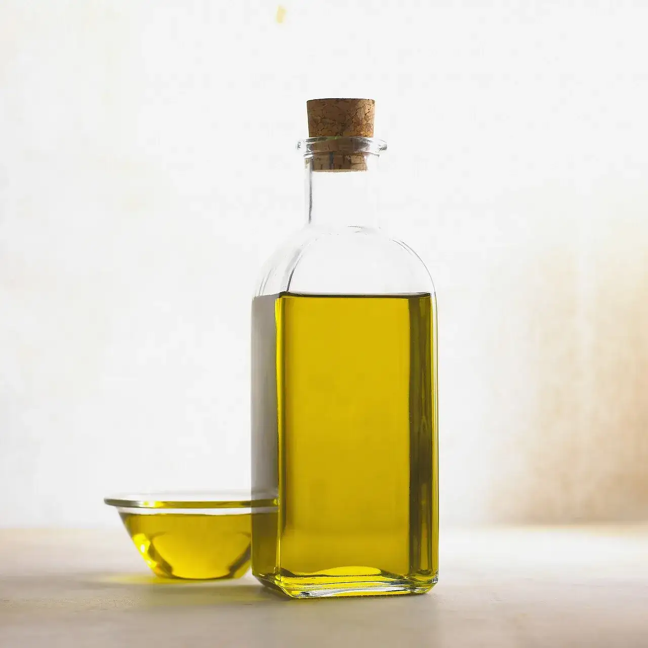 A corked glass bottle of olive oil beside a small dish of the oil