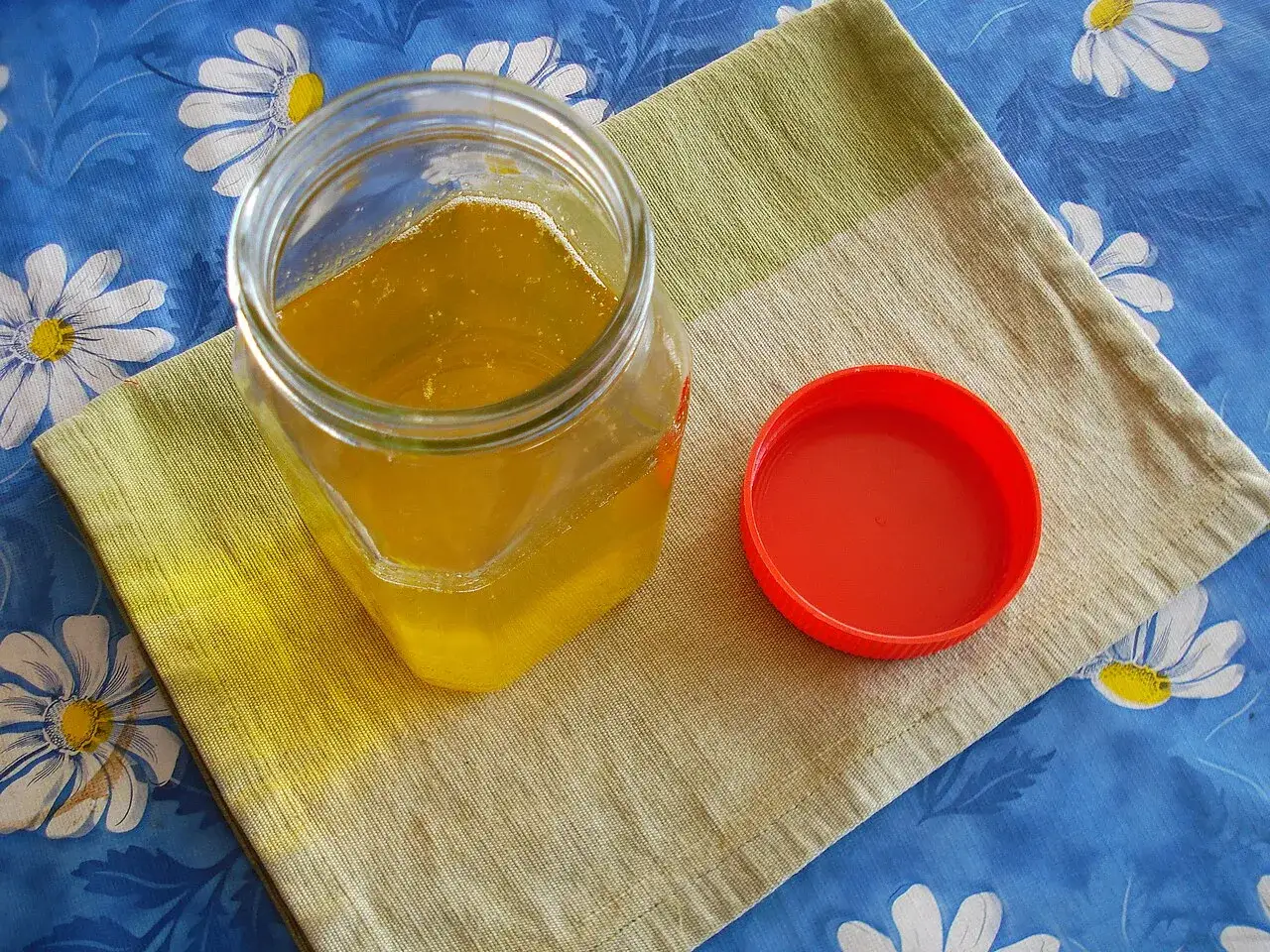 A jar of desi ghee, melted and clear golden, with its red lid beside it