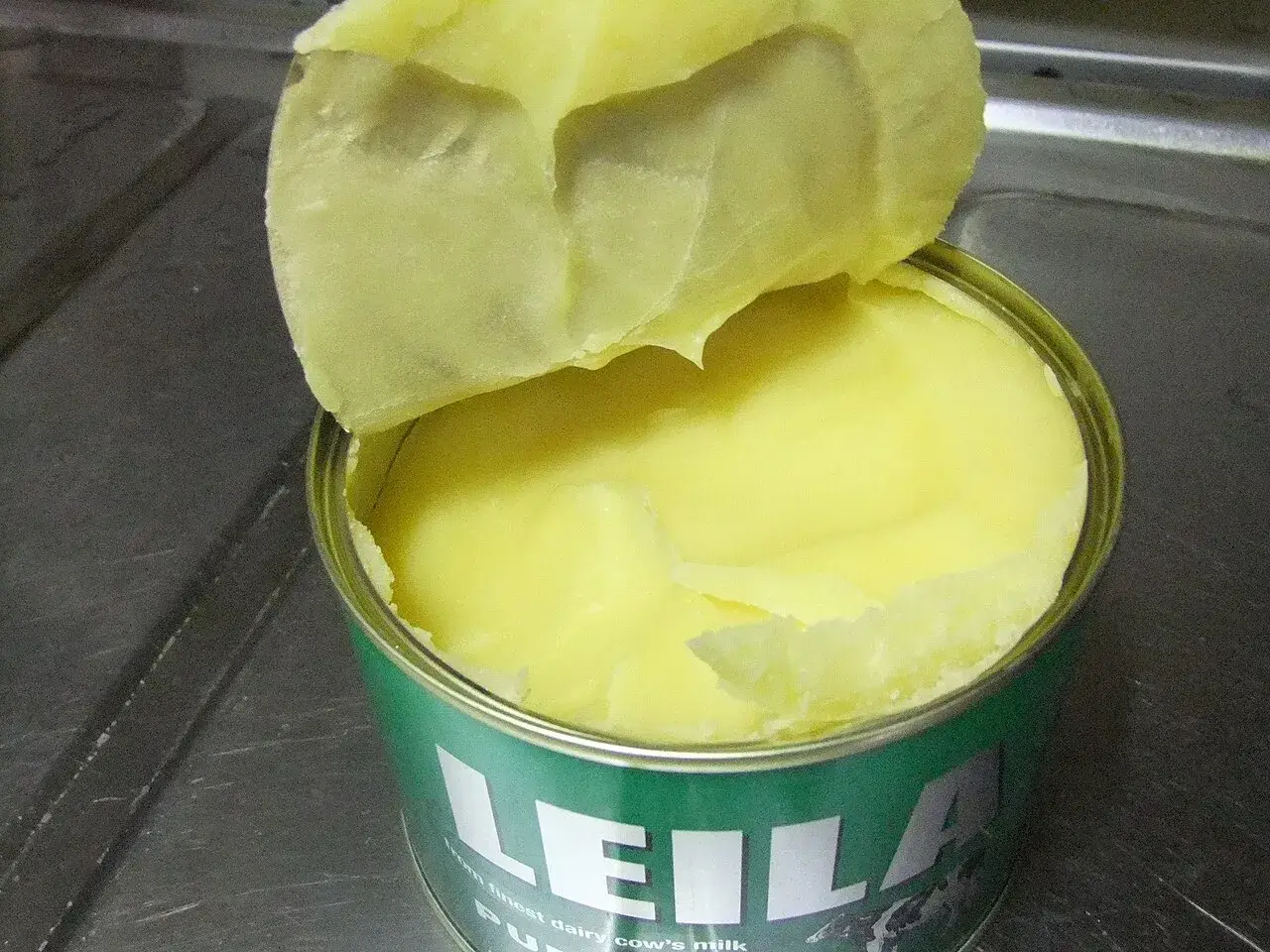 An opened tin of ghee, the surface of the set butterfat visible under the paper seal