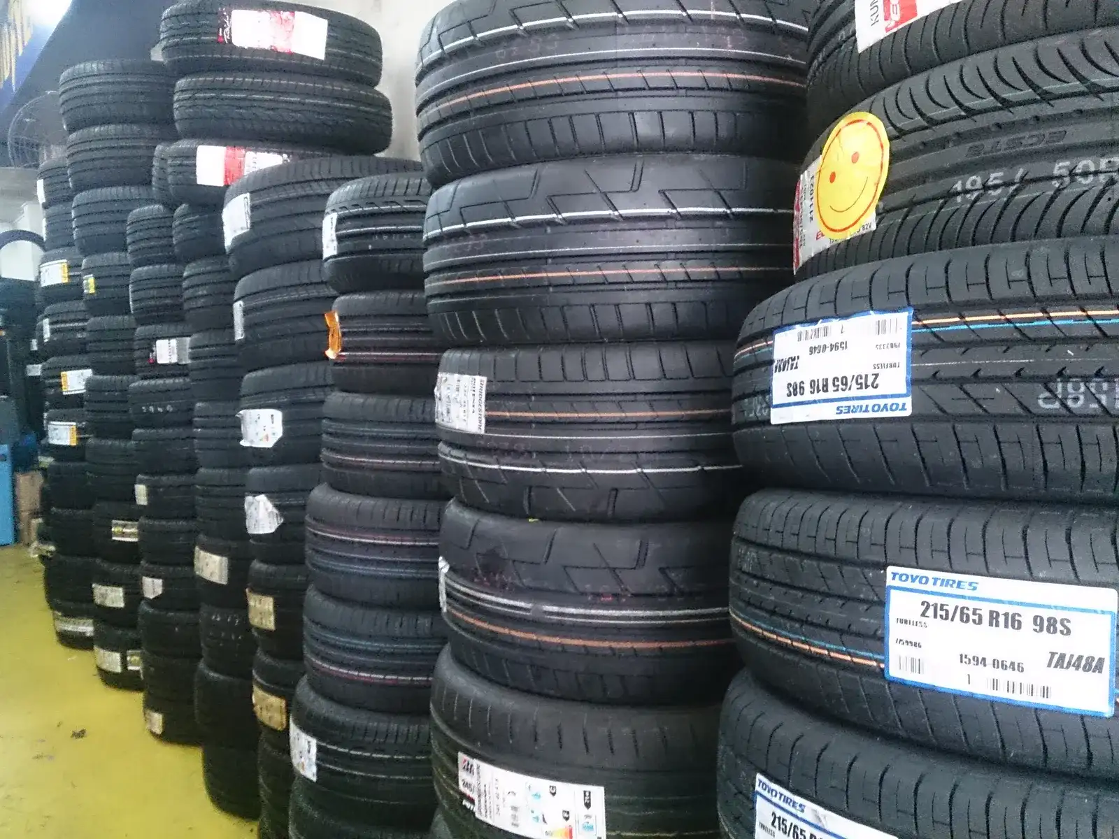 New passenger car tyres stacked in a wholesale rack, each labelled with its size
