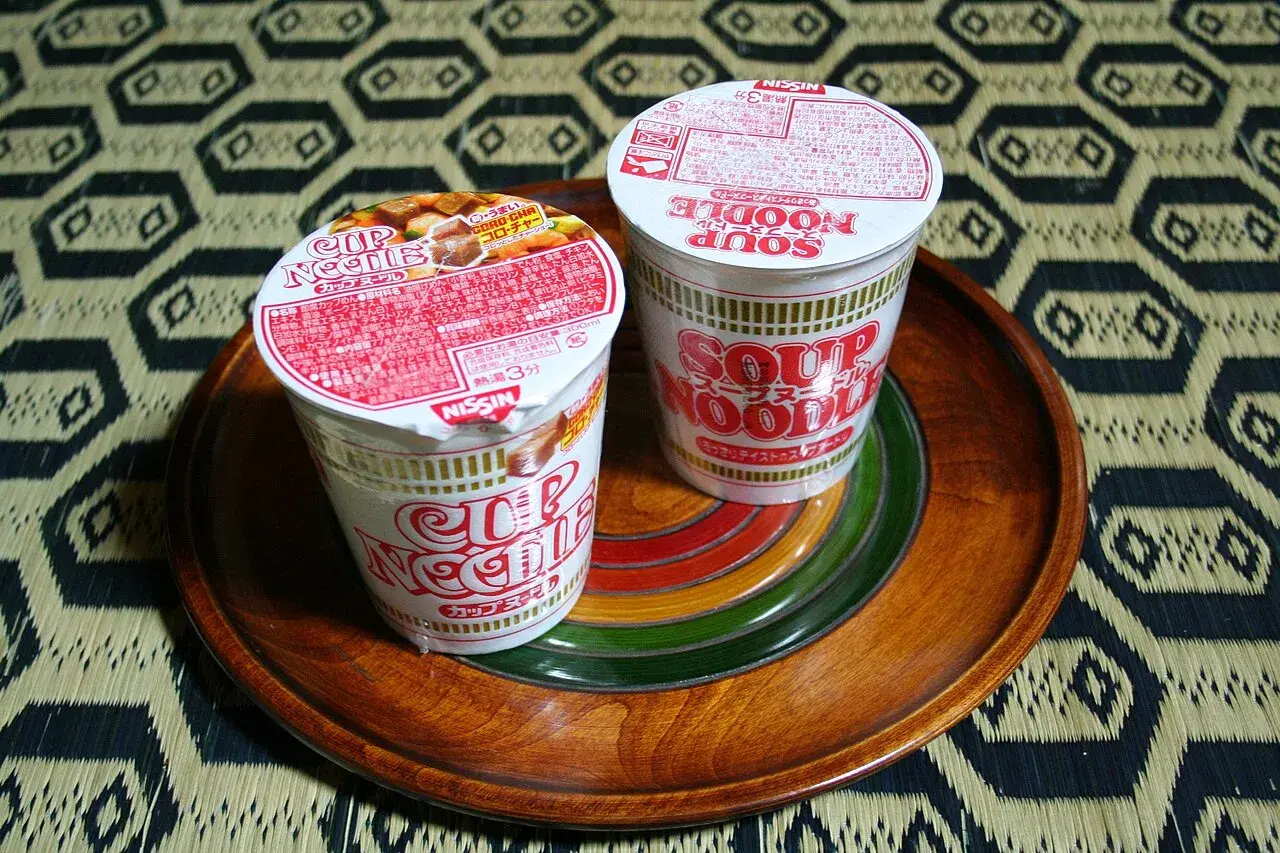 Two Nissin cup noodle cups standing on a tray, lids sealed