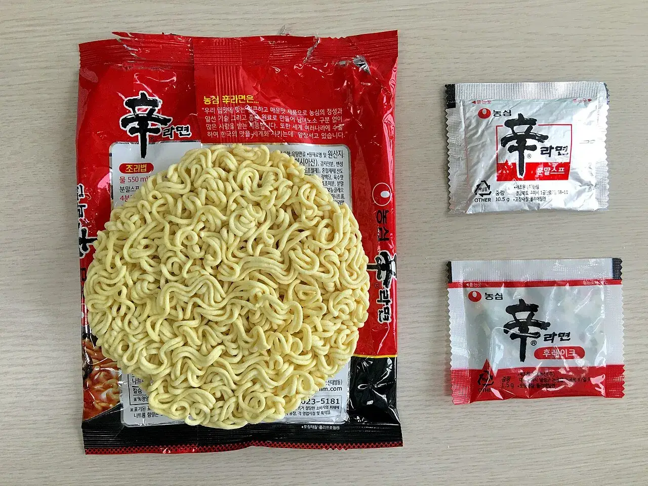 A Nongshim Shin Ramyun pouch with its noodle block and the soup base and vegetable sachets laid out beside it