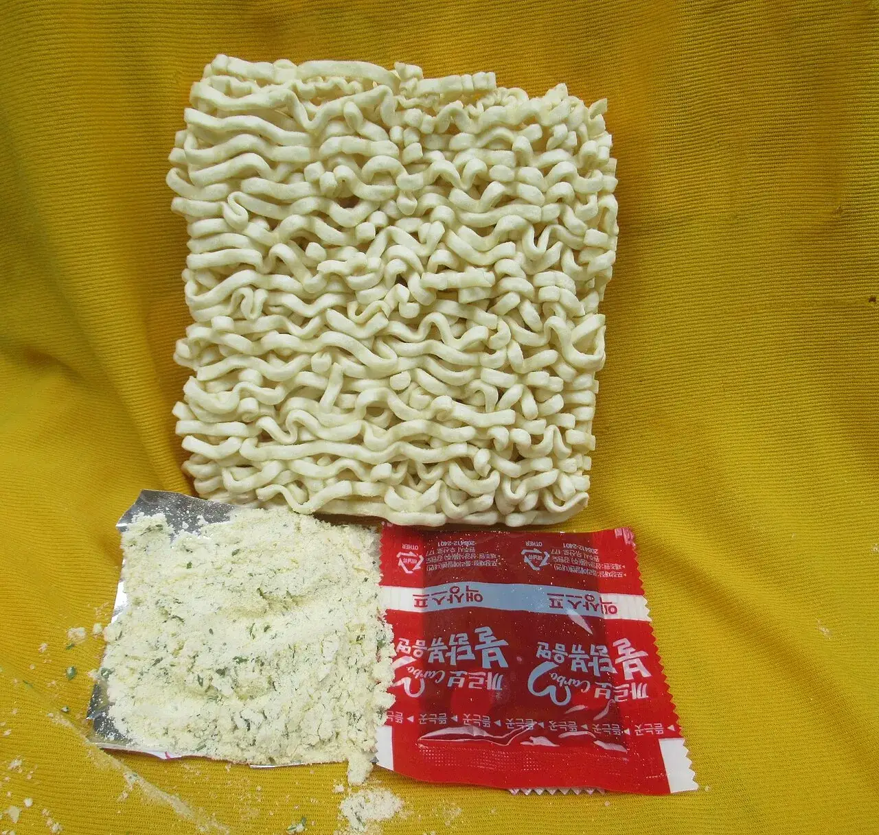The contents of a Samyang Buldak Carbonara pack — the noodle block with its sauce sachet and cheese powder