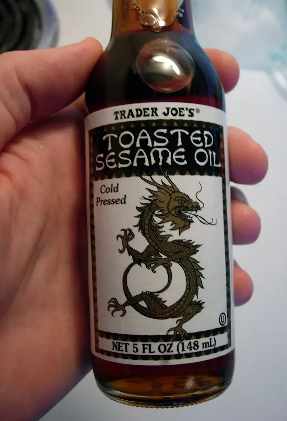 A bottle of toasted sesame oil held in the hand, the dark oil visible through the glass